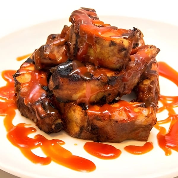 Grilled ribs with a generous coating of red barbecue sauce, served on a white plate.